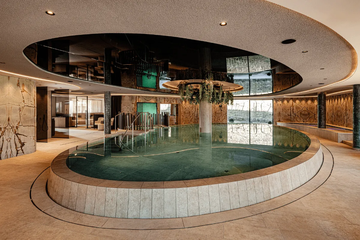 Rundes Hallenbad mit Steineinfassung, Holzverkleidung und einer begrünten Säule in der Mitte