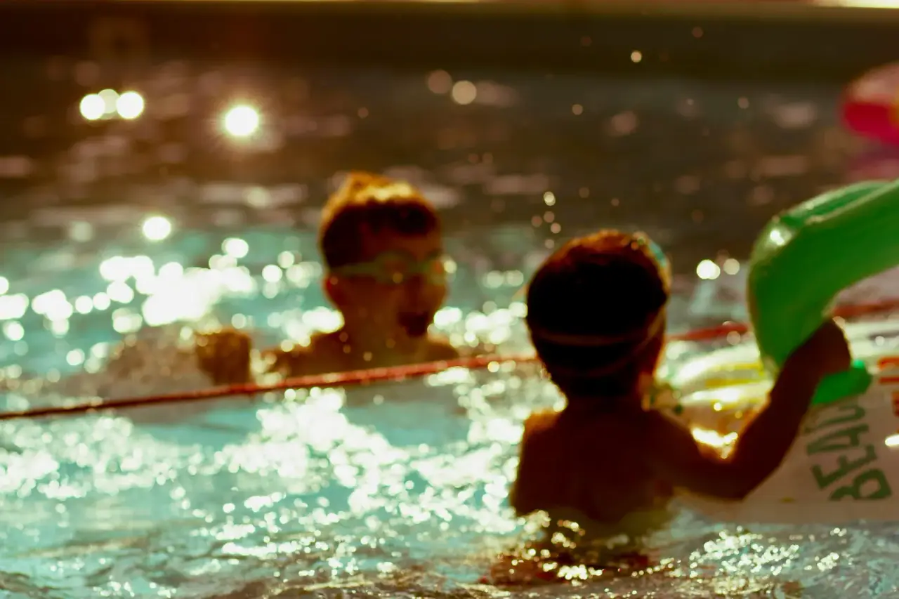 Zwei Kinder mit Schwimmbrillen planschen im Abendlicht im Freibad