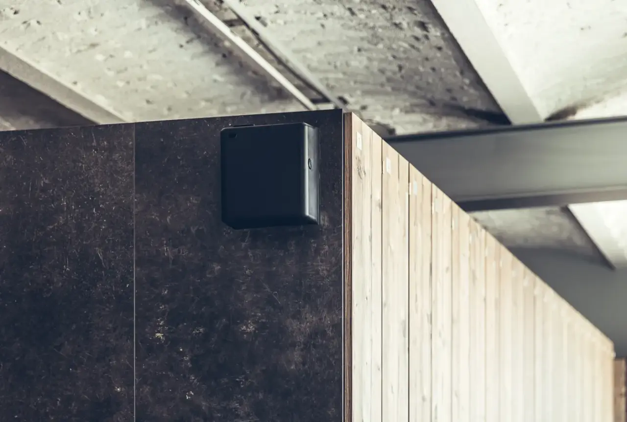 Schwarzes AROMEA Pro Wandgerät an einer dunklen Steinwand neben einer Holzverkleidung