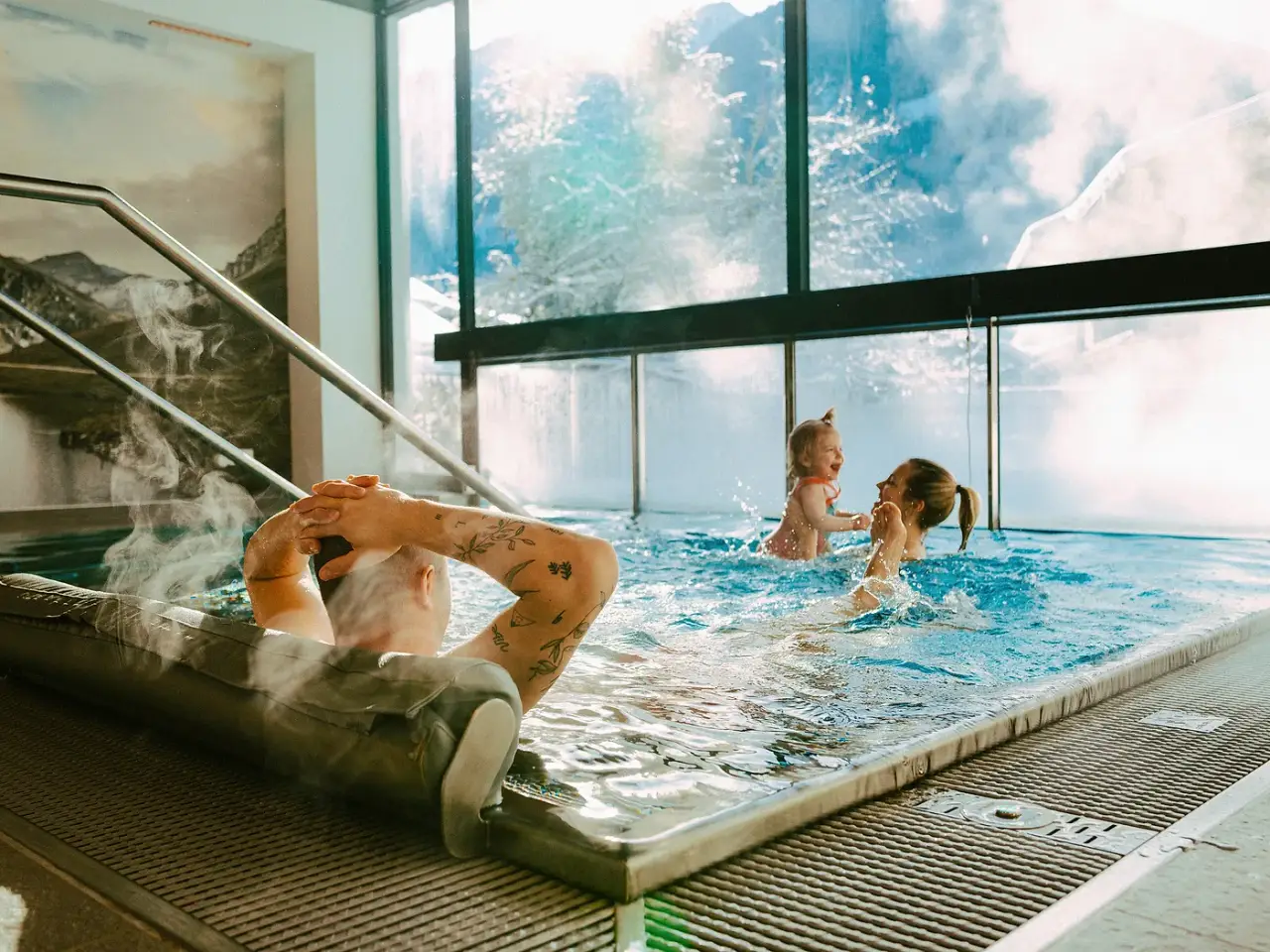 Familie im dampfenden Innenpool der Venediger Lodge, dahinter die verschneite Bergwelt